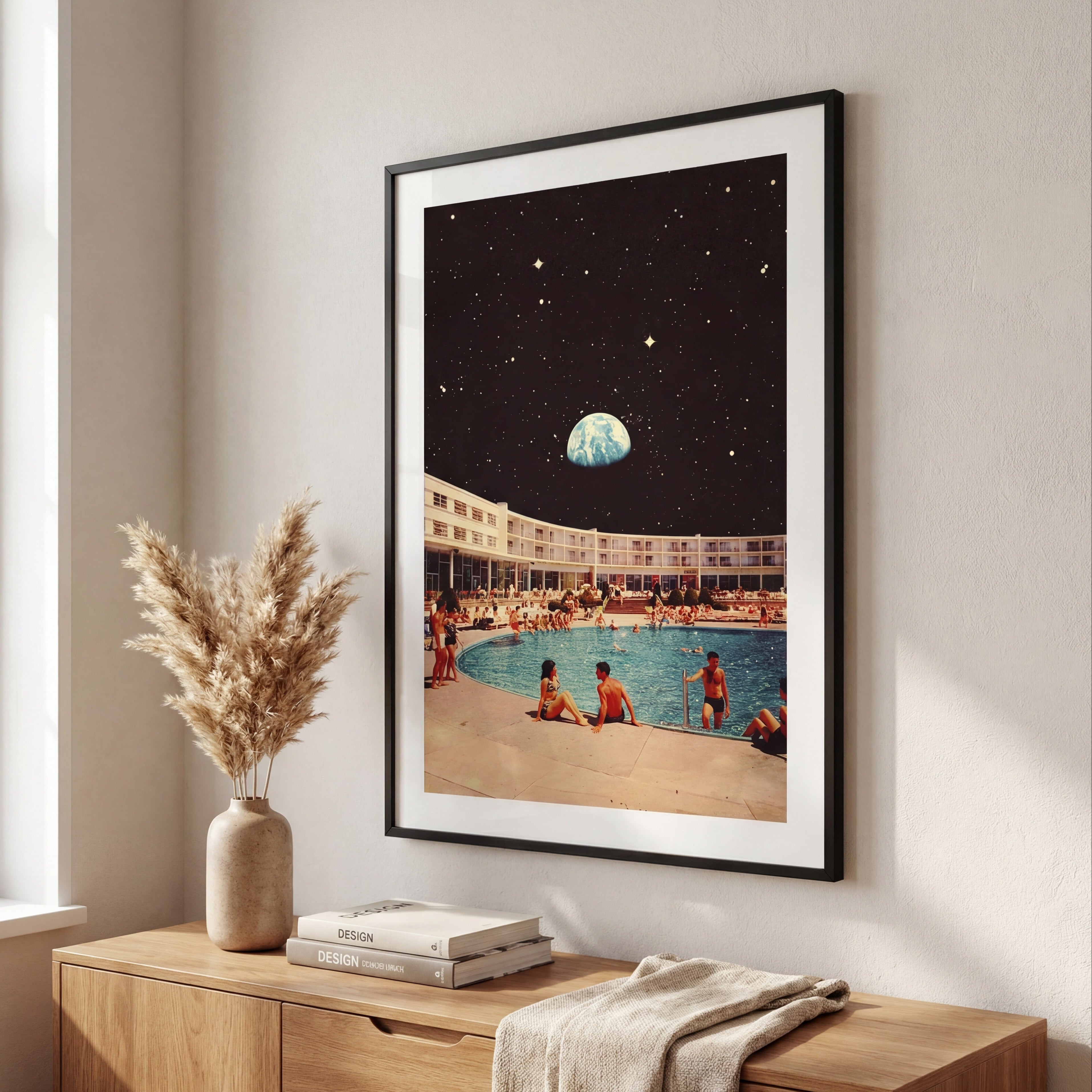 Framed artwork of a poolside scene with people and a planet, above a wooden console table.